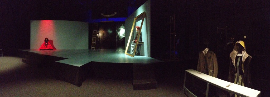 Eine Bühne mit zwei Puppen/Schauspielern. Im Hintergrund steht eine Leiter. Rechts ein großer Bilderrahmen in dem eine Pupper sitzt.
