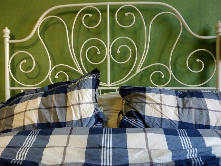 Weißes Bett mit blauen Bettbezug vor olivgrüner Wand