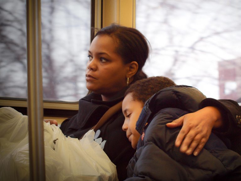 Ein Kind lehnt sich während der Busfahrt an seine Mutter, die aus dem Fenster schaut und es umarmt