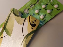 Pille: grüne Pillenpackung mit Wochentagen beschriftet halb verdeckt von weiß-grüner Pillentasche