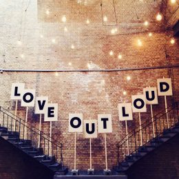 Zwei Treppen links und rechts auf dem Schilder mit einzelnen Buchstaben stehen. Man kann "Love out Loud" lesen. Oben hängen viele kleine, leuchtende Glühbirnen.