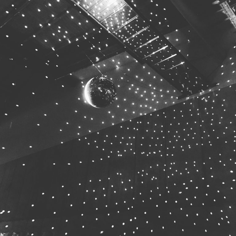 Schwarzweißbild einer Diskokugel, die viele kleine Lichter auf die Wänder wirft