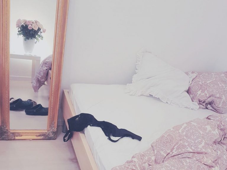 Aufgeschlagenes Bett darauf ein schwarzer BH, daneben ein goldener Spiegel