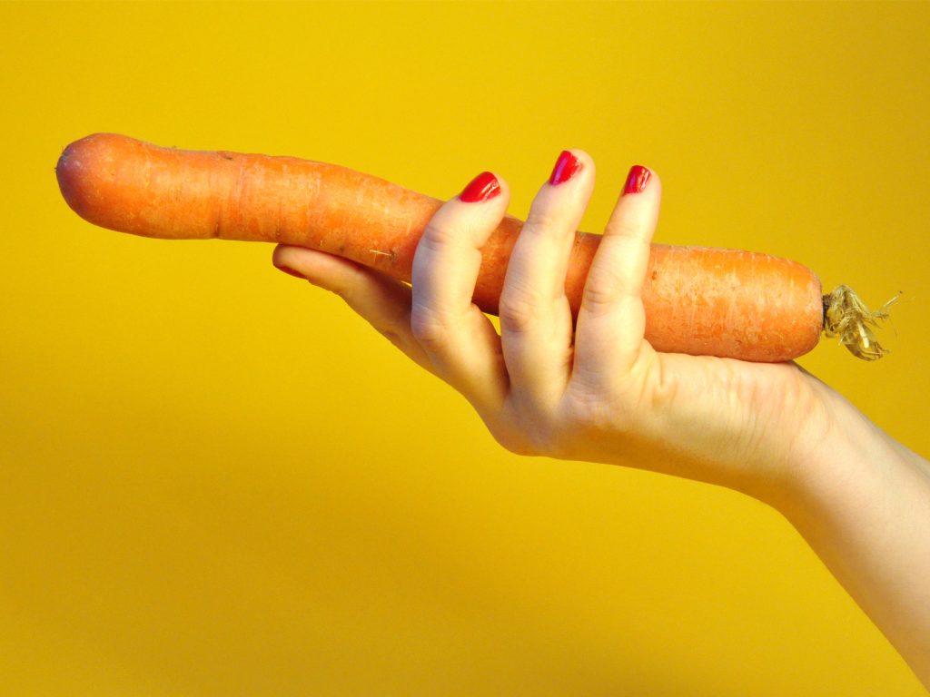 Hand mit Karotte vor Gelb