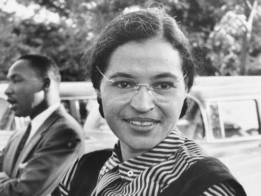 afroamerikanische Frau mit Brille sitzt im Vordergrund, hat eine getreifte Bluse an, im Hintergrund sitzt ein afroamerikanischer Mann seitlich zu der Frau, Rosa Parks