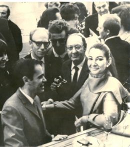 Schwarz Weiß Fotot von Maria Callas, die zwischen vielen Männern an einer Theke steht