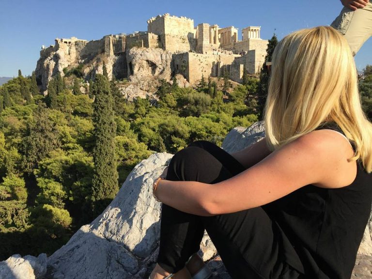Frau sitzt auf einem Stein und schaut auf die Akropolis