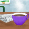 Ein lilafarbiger Becher mit Kaffee steht auf einem Tisch. Daneben liegt eine Zeitung. Im Hintergrund sieht man zwei lila Stuhllehnen und einen Ausschnitt eines Fensters