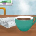 Ein türkisfarbender Becher mit Kaffee steht auf einem Tisch. Daneben liegt eine Zeitung. Im Hintergrund sieht man zwei lila Stuhllehnen und einen Ausschnitt eines Fensters