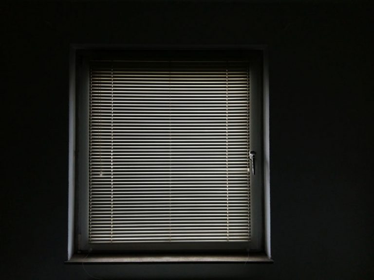 Ein Foto eines Fenster. Die Jalousie ist runter gelassen. Licht wird durch die Lamellen geworfen
