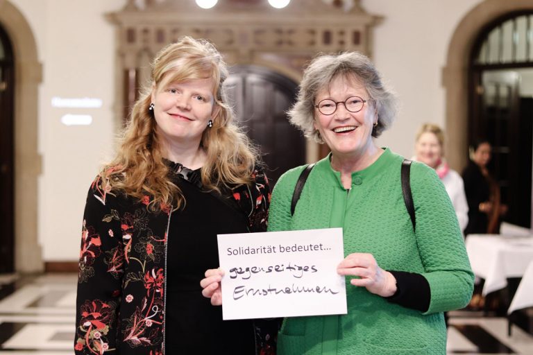 Ulrike Hauffe und Renate Strümpel mit einem Zettel, auf dem steht "Solidarität bedeutet..gegenseitiges Ernstnehmen"