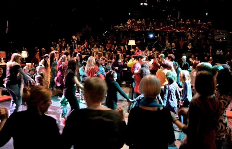 Eine Gruppe tanzender Frauen im Hintergrund ein Orchester