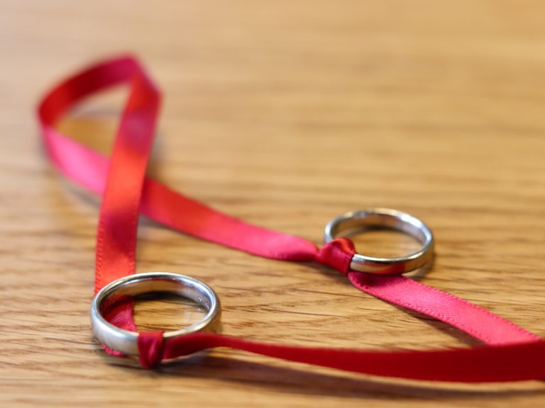 Zwei Eheringe sind mit einem roten Stoffband verknotet.