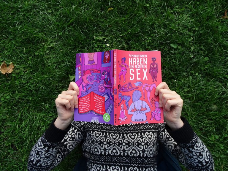 Person liest auf einer Wiese die Graphic Novel "Feministinnen haben den besseren Sex" von Flo Perry