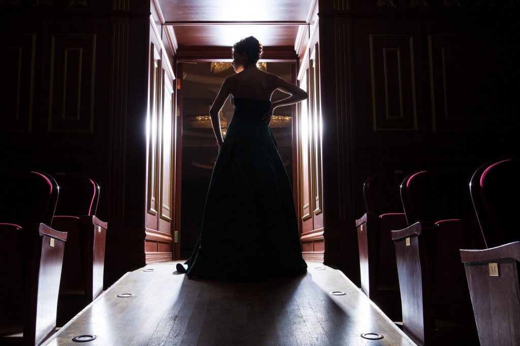 Rückansicht einer Frau im Kleid im Gegenlicht, in einer Theatertür stehend