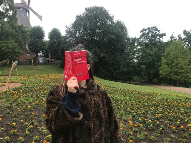 Ein Mädchen steht mit dem Buch "Reproduktive Freiheit" (Schrupp) vor der Mühle in Bremen