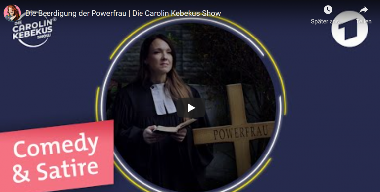 Carilin Kebekus ist als Pristerin neben einem Kreuz zu sehen auf dem Powerfrau steht