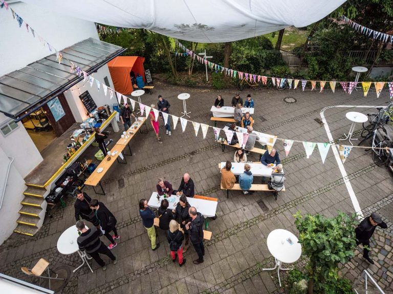 Blick auf einen Innenhof mit Wimpeln im Künstlerhaus Bremen, Menschen stehen an Tischen