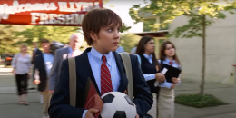 weiblich gelesene Person an Jungenhighschool mit Schuluniform und Fußball in der Hand, soll als Junge verkleidet sein 