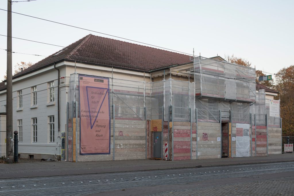 Außenansicht Willhelm-Wagenfeld-Haus mit dem Plakat der Ausstellung Architektur für Alle? und Baugerüst