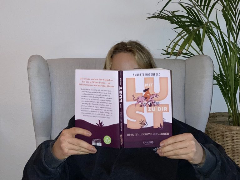 Rezipientin sitzt auf einem Sessel und liest das Buch "Mit Lust zu Dir - Sexualität als Schlüssel zur Selbstliebe" von Annette Hosenfeld.