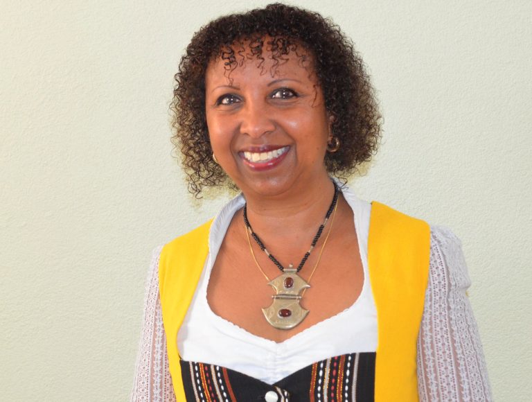 Schwarze Frau im Porträt, lächeld mit großer Kette und Locken