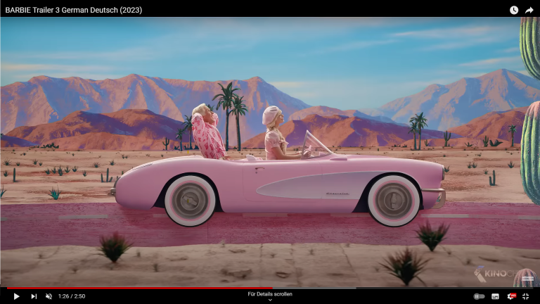 Das Bild zeigt Barbie und Ken in einem pinken Cabrio, auf einer Straße in der Wüste. Barbie fährt und Ken sitzt auf dem Rücksitz.