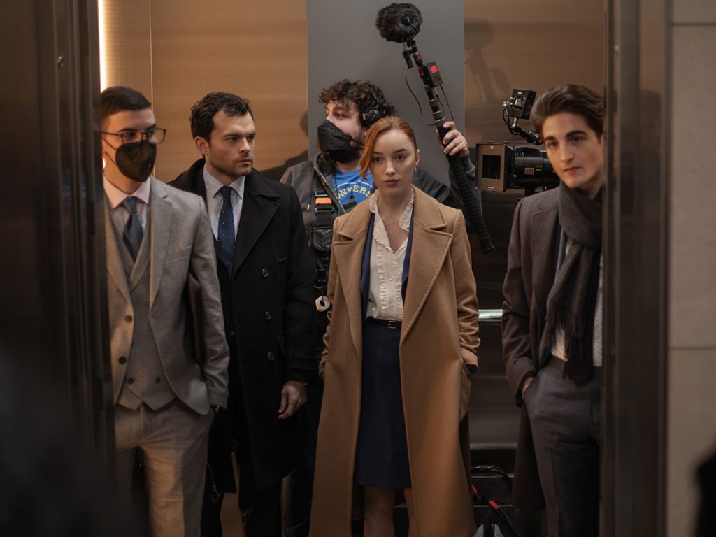 Behind The Scenes Foto der Netlfix-Serie "Fair Play". Man sieht die Schauspielerin Phoebe Dynevor in einem Fahrstuhl stehen. Um Sie herum stehen 3 Männer und ein Kameramann der ein Mikro nach oben hält.