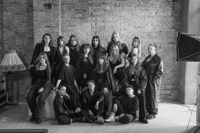 Auf diesem schwarz-weiß Foto sind fünfzehn Frauen zu sehen, die alle ernst in die Kamera schauen und hintereinander stehen oder sitzen.