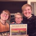Drei Frauen strahlen in die Kamera über einem Titelblatt des Weser Kuriers.
