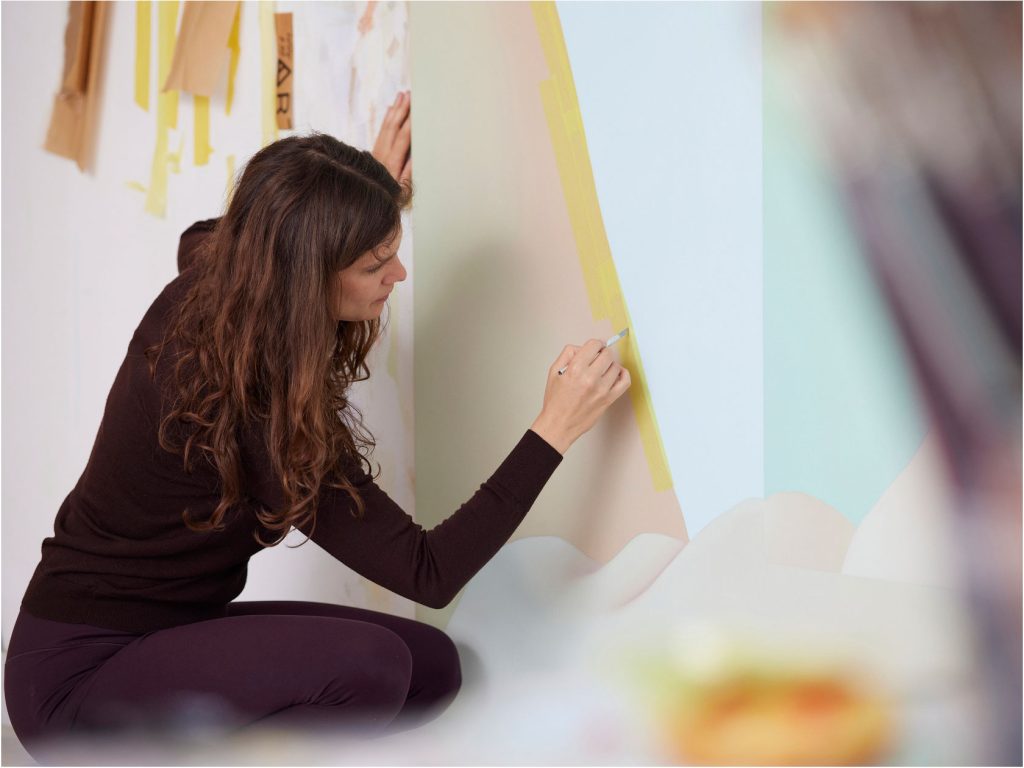 Die Künstlerin Vivian Greven sitzt in der Hocke vor einer Leinwand und setzt einen Pinselstrich.